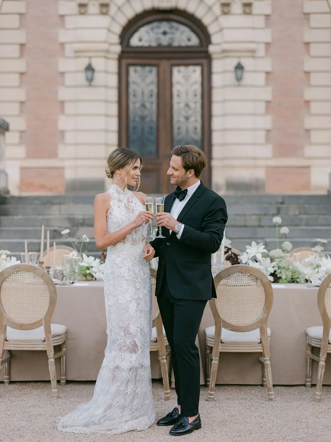 A bride and groom toasting before an elegant reception table at a French château